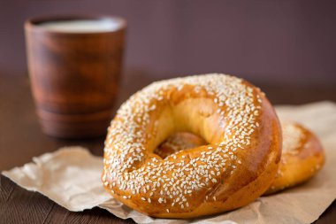 İki simit susam ile ve koyu ahşap bir masa üzerinde süt fincan. Görünümü yan, yakın çekim.