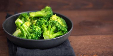 Taze yeşil brokoli kahverengi ahşap zemin üzerinde siyah plaka üzerinde.