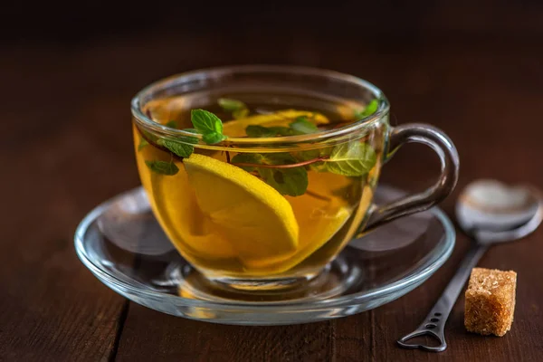 Cup of Lemon tea with lemon slices, cane sugar and mint on dark wooden background.