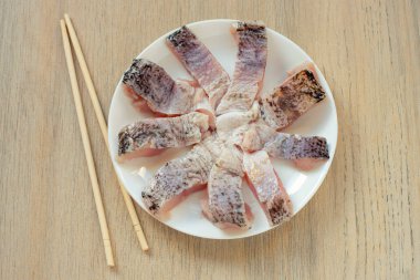 Hafif bir arka plan üzerinde yemek çubukları ile beyaz plaka üzerinde çiğ balık dilimlenmiş.