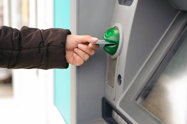 Hand inserting ATM card into bank machine to withdraw money.