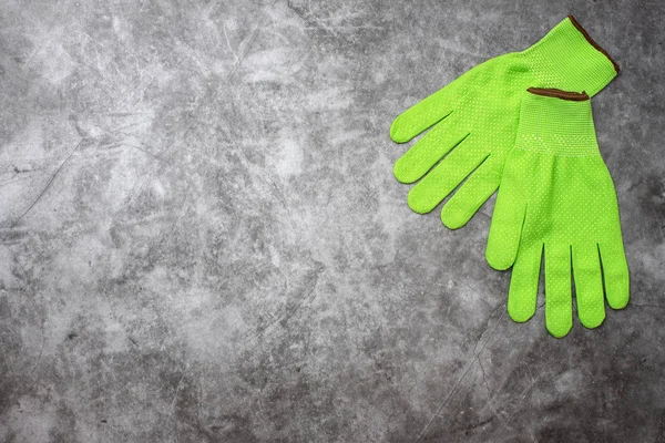 Green work gloves on grey background. Top view, with copy space.