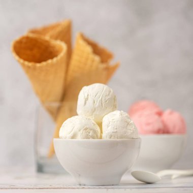 Vanilya ve pembe çilek dondurma ve waffle koniler ışık arka plan üzerinde kase. Yan görünüm.