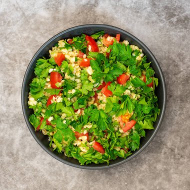 Bulgur ile Tabbouleh salata, maydanoz, bahar soğan ve domates gri arka planda kase. Üst görünüm