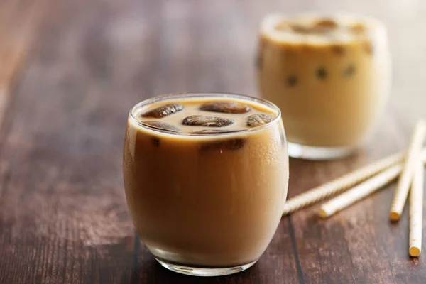 Milk coffee cocktail in glasses with frozen coffee cubes on wooden table. Side view