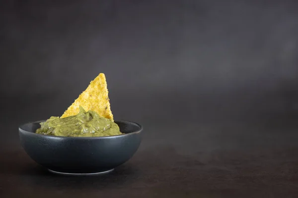 Grön Guacamole med nachos i skål på mörk bakgrund — Stockfoto