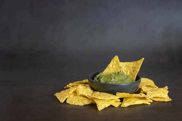 Grön Guacamole med nachos i skål på mörk bakgrund — Stockfoto