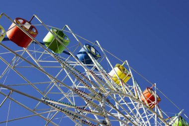 Dönme dolabın bir kısmı mavi gökyüzüne karşı aşağıdan vurulmuş. Öğlen parkta.