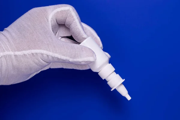 Beyaz steril eldivenli bir adamın eli aşağıya doğru eğimli plastik beyaz bir burun spreyi tutar..