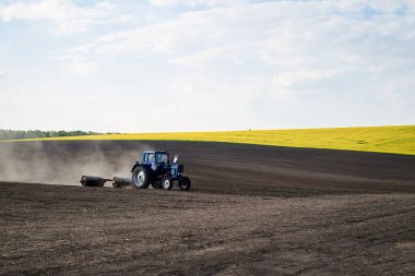 Kara topraklarla tarımsal işler. Mavi traktör biniciliği ve tohum ekme kırsalında. Kırsal bölgeler ilkbaharda çalışır. Çevre koruma kavramı. Ekolojik ürünler yetiştirme. Doğal arkaplan.
