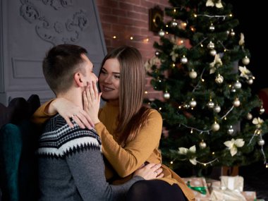 Birbirine aşık genç bir çift Noel ağacının yanında şöminenin başında oturmuş randevularında öpüşüyorlar. Yakışıklı esmer adam, gri kazak giyiyor, hardal sarısı örgü elbiseli güzel kadını öpüyor..