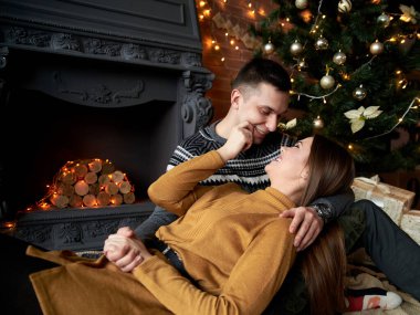 Gri kazaklı yakışıklı esmer adam ve hardal sarısı örgü elbiseli genç kadın Noel ağacının yanındaki yerde, sarılıyorlar. Şöminenin yanında birbirine aşık bir çift, tuğla duvarlı karanlık bir odada