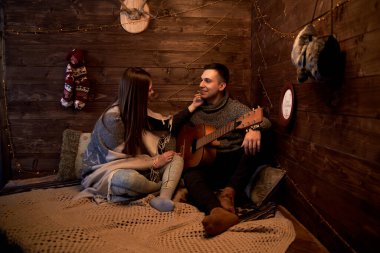 Yeni yıl arifesinde ahşap oda kulübesinde romantik bir randevuya çıkan genç çift. Gri kış kazağı giyen esmer adam, sıcak battaniyeyle örtülü güzel bir kadın için gitar çalıyor..