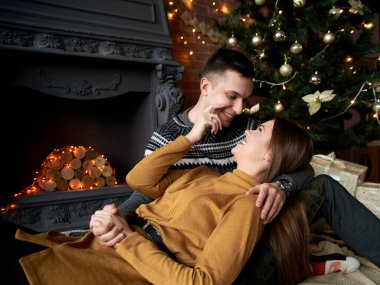 Gri kazaklı yakışıklı esmer adam ve hardal sarısı örgü elbiseli genç kadın Noel ağacının yanındaki yerde, sarılıyorlar. Şöminenin yanında birbirine aşık bir çift, tuğla duvarlı karanlık bir odada