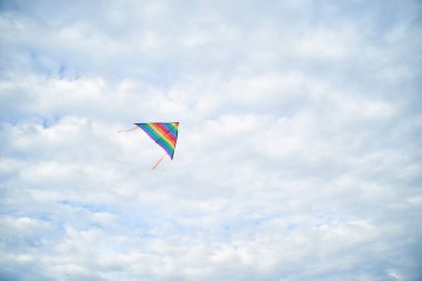 Yazın açık mavi bulutlu gökyüzünde uçan renkli gökkuşağı uçurtması. Aile eğlencesi aktivitesi. İlkbahar yaşam tarzınız kutlu olsun. Çocuk oyuncakları. Gökyüzü manzarası arka planı.