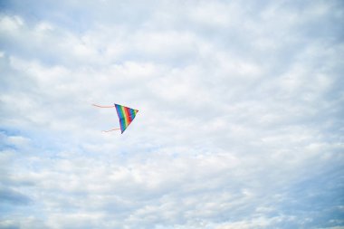 Yazın açık mavi bulutlu gökyüzünde uçan renkli gökkuşağı uçurtması. Aile eğlencesi aktivitesi. İlkbahar yaşam tarzınız kutlu olsun. Çocuk oyuncakları. Gökyüzü manzarası arka planı.