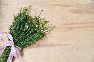Ahşap masa üzerinde pembe kurdeleyle bağlanmış yeşil saplı küçük beyaz papatya çiçekleri. Vahşi çiçeklerin doğal arka plan resmi. Şiirler, mektuplar, romantik notlar için ekolojik doku.