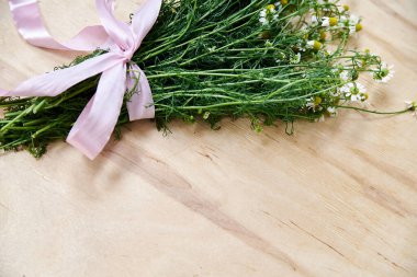 Ahşap masa üzerinde pembe kurdeleyle bağlanmış yeşil saplı küçük beyaz papatya çiçekleri. Vahşi çiçeklerin doğal arka plan resmi. Şiirler, mektuplar, romantik notlar için ekolojik doku.