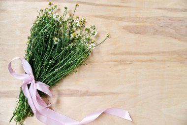 Ahşap masa üzerinde pembe kurdeleyle bağlanmış yeşil saplı küçük beyaz papatya çiçekleri. Vahşi çiçeklerin doğal arka plan resmi. Şiirler, mektuplar, romantik notlar için ekolojik doku.