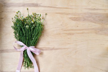 Ahşap masa üzerinde pembe kurdeleyle bağlanmış yeşil saplı küçük beyaz papatya çiçekleri. Vahşi çiçeklerin doğal arka plan resmi. Şiirler, mektuplar, romantik notlar için ekolojik doku.