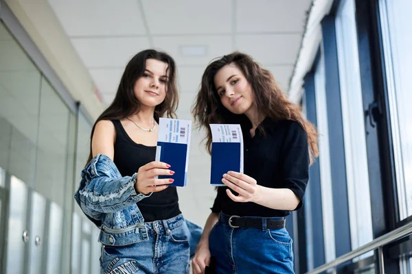 国際パスポートと搭乗券を保持する2人の若いブルネットの女の子のクローズアップ写真は 軽い空港廊下文書管理でチケットを渡します 飛行機で旅する彼女たち — ストック写真