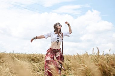 Genç esmer hippi kadınlar, boho tarzı kıyafetler giyiyorlar, buğday tarlasında dans ediyorlar. Kadın doğa aşığı, kırsalda meditasyon yapıyor. Eko turizm konsepti. Yaz tatili boş zaman.