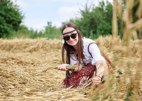 布鲁内特嬉皮士女人 穿着布荷风格的衣服 蹲在黄色的田野上 捡起麦茎 做成天然的花束 在农村旅行的人生态旅游概念 夏季休闲 — 图库照片