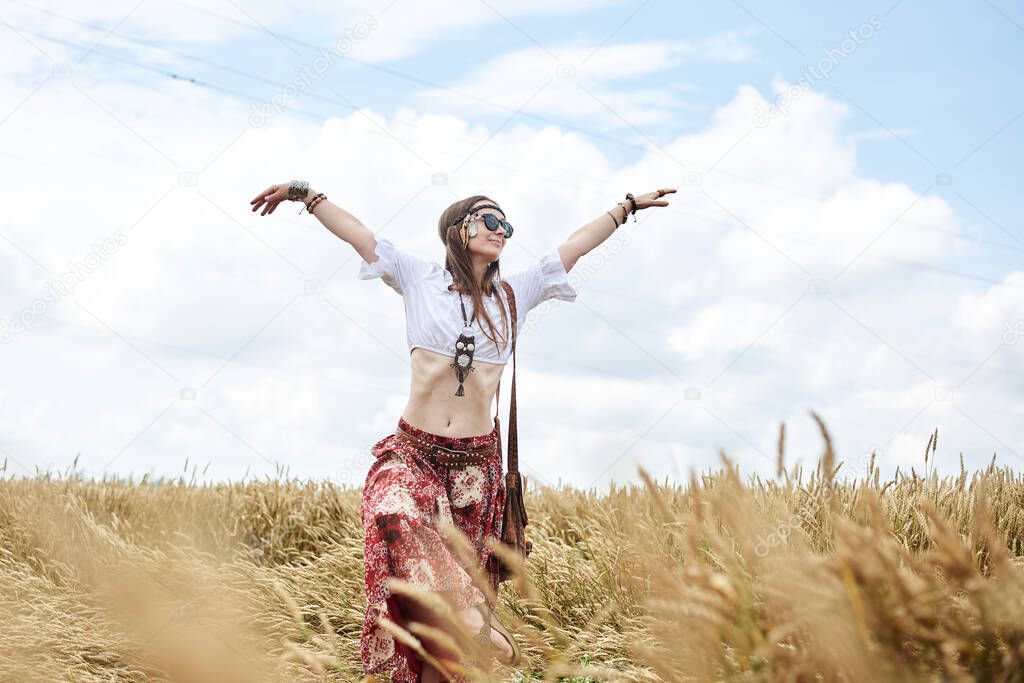 Young brunette hippie women, wearing boho style clothes, dancing in wheat field. Female nature lover, meditating in countryside. Eco tourism concept. Summer leisure free time.