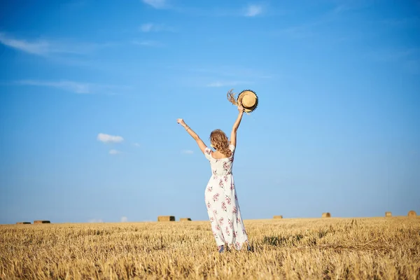 年轻的金发女人 穿着白色的浪漫连衣裙 手持草帽和干草花束 夏天在稻草地里跳跃 自然背景的女性肖像 环境保护 — 图库照片