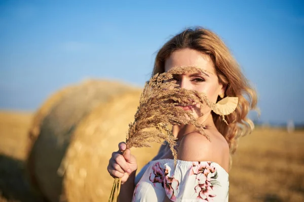 年轻的金发女人 穿着白色的浪漫连衣裙 在夏天 她的脸上挂着干草束 站在田边麦包旁边 自然背景的女性肖像 — 图库照片