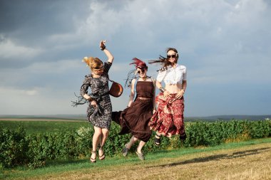 Üç hippi kadın, boho tarzı kıyafetler giyiyorlar, atlıyorlar, yeşil alanda eğleniyorlar. Kırsalda birlikte seyahat eden bayan arkadaşlar. Eko turizm konsepti. Yaz tatili boş zaman.