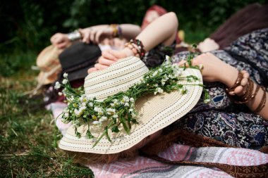 Üç hippi kadın, renkli boho tarzı kıyafetler ve hasır şapkalar giyiyorlar güneşli yaz gününde yeşil çimlerde uzanıp dinleniyorlar. Kırsal kesimde çevre turizmi. Birlikte seyahat eden arkadaşlar..