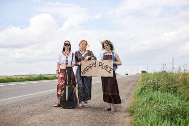 Üç hippi kadın, boho tarzı kıyafetler giyiyorlar, yolda dikiliyorlar, başparmak gezdiriyorlar, kartonda Happy Place yazan bir yere otostop çekiyorlar. Arkadaşlar, yazın birlikte seyahat ediyoruz. Özgürlük ve mutluluk kavramı.