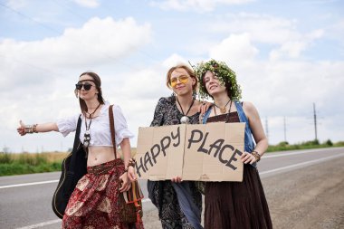 Üç hippi kadın, boho tarzı kıyafetler giyiyorlar, yolda dikiliyorlar, başparmak gezdiriyorlar, kartonda Happy Place yazan bir yere otostop çekiyorlar. Arkadaşlar, yazın birlikte seyahat ediyoruz. Özgürlük ve mutluluk kavramı.