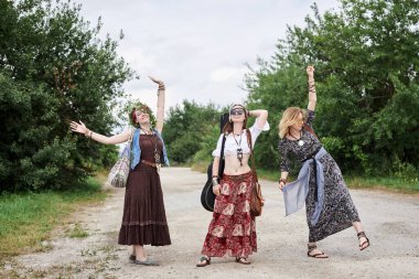 Üç hippi kadın, boho tarzı kıyafetler giyiyorlar, kırsalda toprak yolda yürüyorlar, dans ediyorlar, dinleniyorlar, eğleniyorlar. Arkadaşlar, yazın birlikte seyahat ediyoruz. Özgürlük ve mutluluk kavramı.