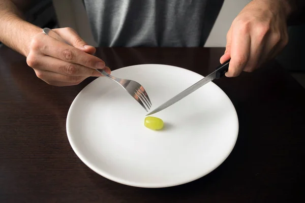 Healthy food theme: hands holding knife and fork on a plate with green grape on a white plate