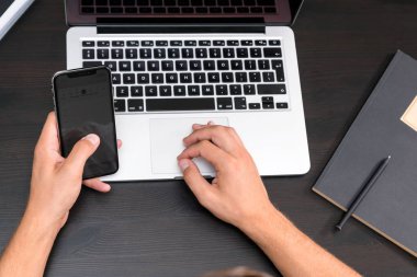 Antika ahşap masa dizüstü bilgisayar üzerinde çalışırken akıllı telefon yazarak eller mans. Tipik bir klavye üzerinde eller. Üstten görünüm, iş Ofis İşyeri