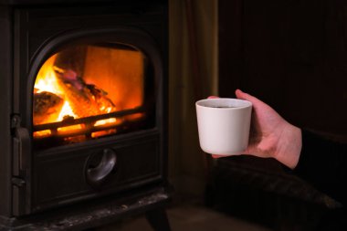 Bir fincan sıcak şömine pistte sahip bir kadın. Ahşap günlükleri içe yanar artalanda ile yanan şömine. Sıcak ışık, Romantik, Noel atmosfer gibi 