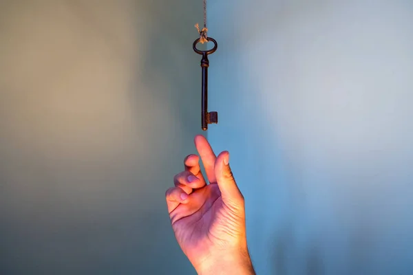 People hand reaching for vintage key hanging on a string. Business success freedom concept concept for aspirations, achievement and incentive