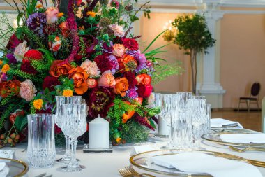 Düğün masa dekorasyonu. Güzel tabak, kristal bardak ve tabaklar yanındaki masaya çiçek buketi
