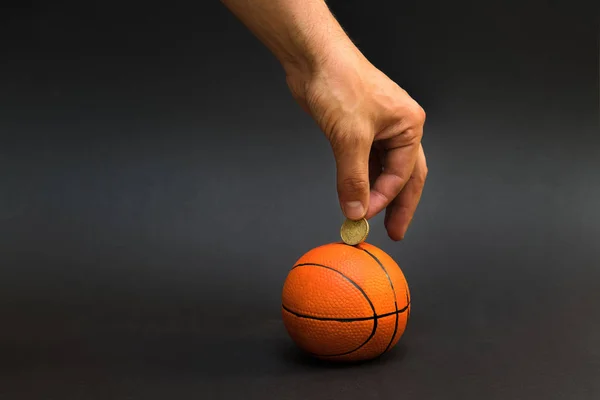 Mužské ruky uvádění mince do prasátko s tvarem basketbal izolovaných na černém pozadí — Stock fotografie