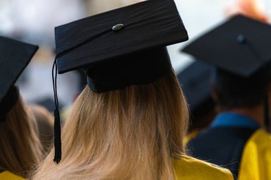 Önlük ve kapalı oturmuş, diploma, almak için beklediğini şapka giyen öğrenciler üniversite, kolej mezuniyet mezuniyet günü