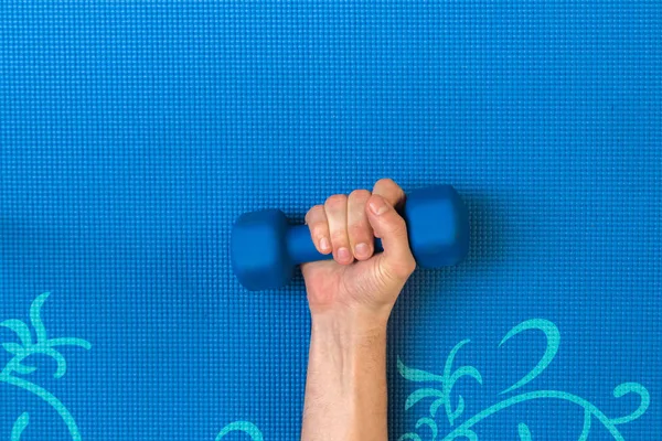 Hand holding light weight on top of yoga mattress. Exercising, healthy lifestyle background