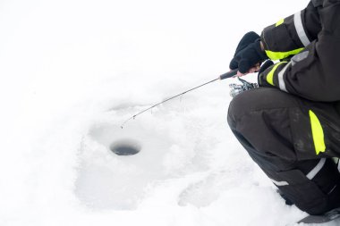 Buzda kış balıkçılığı. Buz deliğinde yem sallayan bir adam. Vahşi doğada dinleniyor