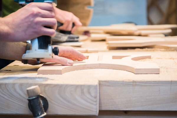 Young carpenter grinding cut out food decoration with electric sandpaper machine