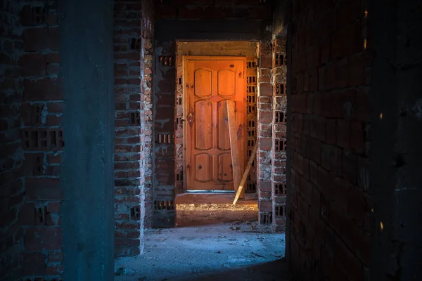 Antiguo, aterrador, abandonado interior de la casa. Puerta de madera al final del pasillo de hormigón aterrador. Estructura arquitectónica — Foto de Stock