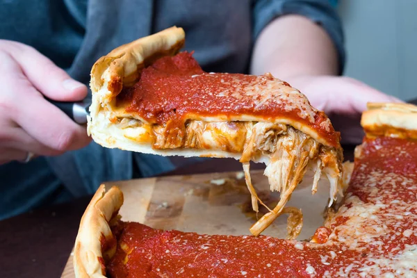 Chicago pizza üst görünümü. Kadın elleri domates sosu ve sığır eti ile Chicago tarzı derin çanak İtalyan peynir pizza kesme içinde karşılamak