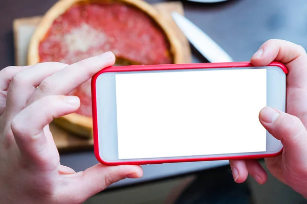 Top view of Chicago pizza. Woman hands taking photo with smart phone of Chicago style deep dish italian cheese pizza with tomato sauce and beef meet inside. Blank, empty screen