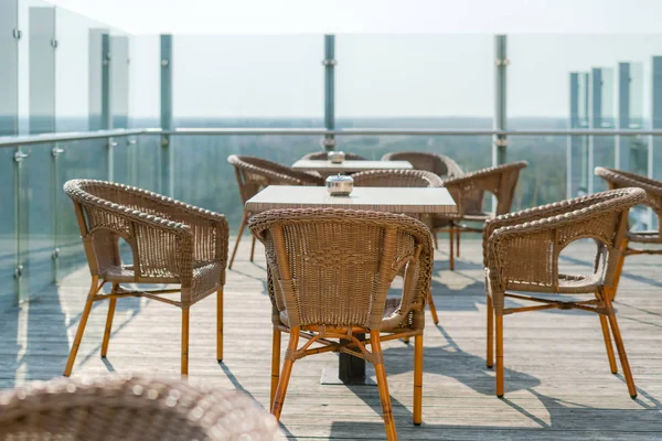 Empty cafe with rattan wicker armchairs and tables on summer garden terrace outdoor, free space. Table and chairs in empty cafe. Wicker furniture rattan chairs on terrace