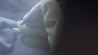 Diş laboratuarında kum blaster kullanarak yapay seramik dişleri parlatma diş teknisyeni. Profesyonel elinde sahte dişler tutarak ve kum blaster ile parlatma sırasında eldiven giyiyor